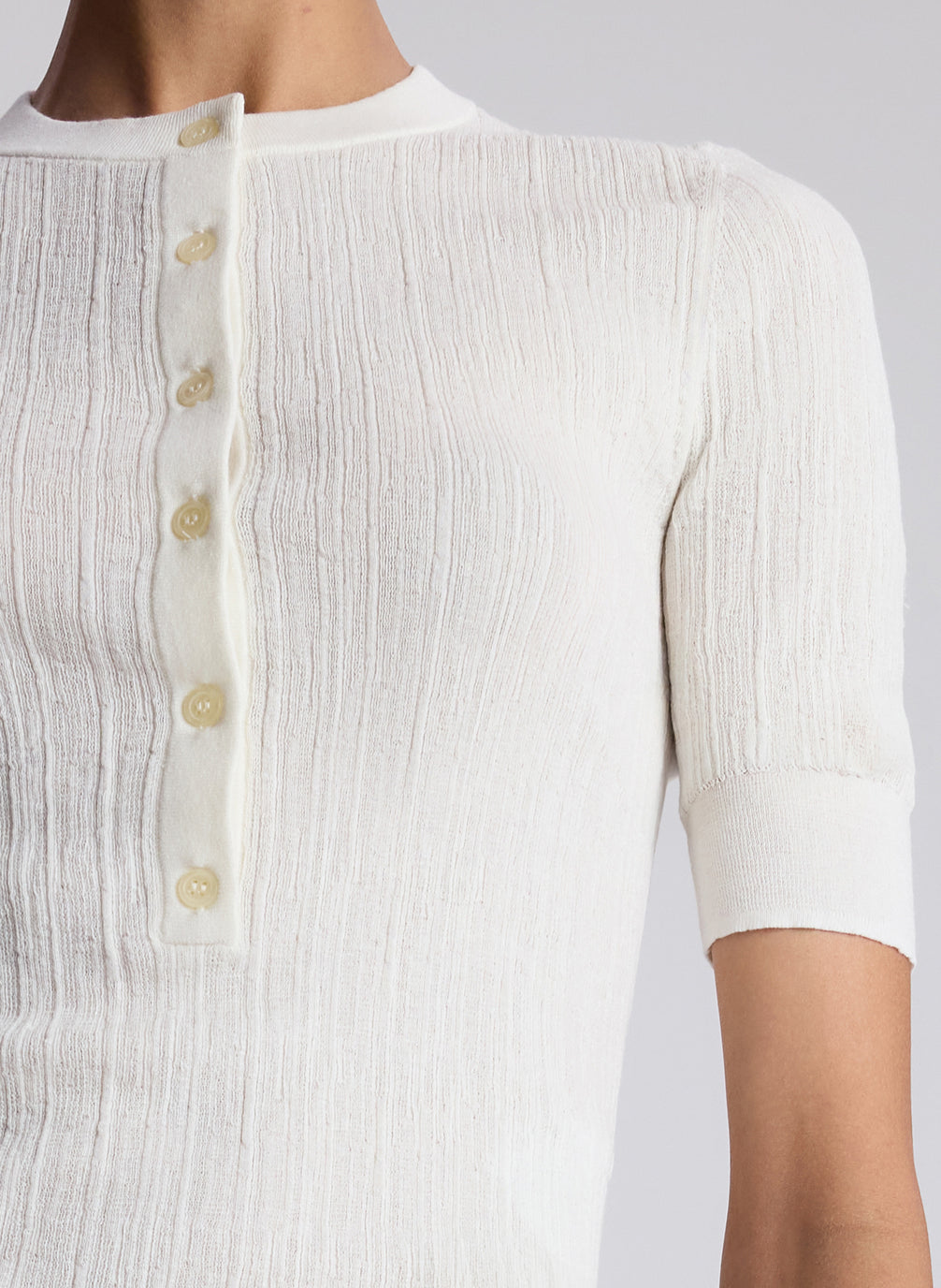 Close-up of a white textured shirt with buttons on a plain background