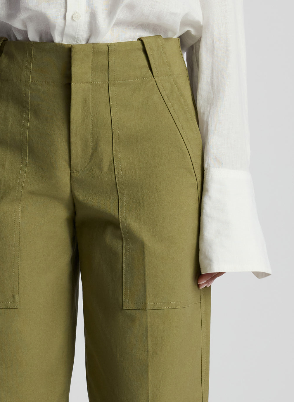detail view of woman wearing white button down shirt and olive pants