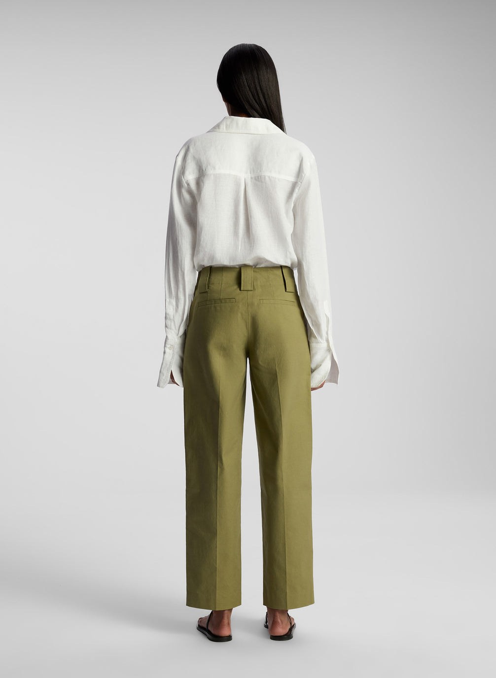 back view of woman wearing white button down shirt and olive pants