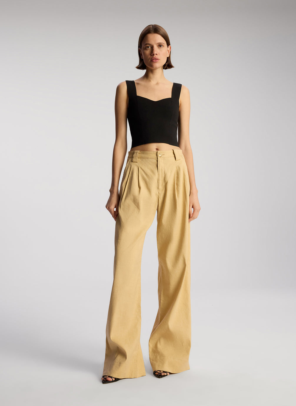 front view of woman wearing black sleeveless compact knit top and tan pants