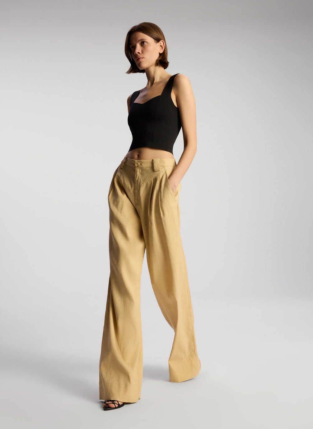 side view of woman wearing black sleeveless compact knit top and tan pants