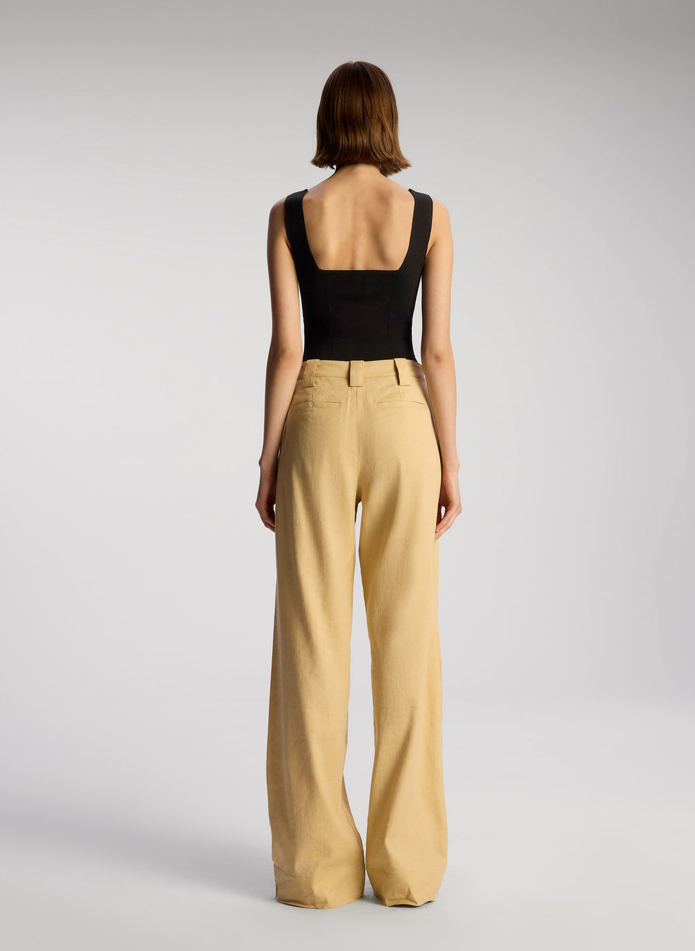 back view of woman wearing black sleeveless compact knit top and tan pants