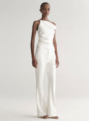 Woman wearing a white one-shoulder top and white pants on a plain background