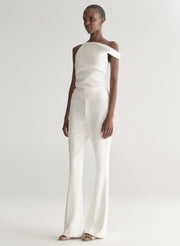 Woman wearing a white one-shoulder top and white pants on a plain background