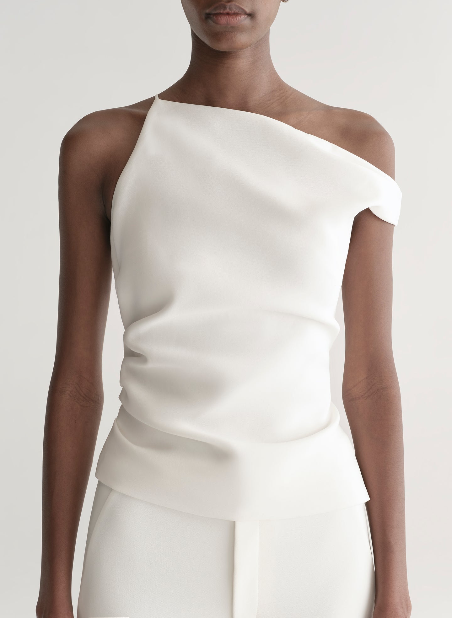 Woman wearing a white one-shoulder top and white pants on a plain background