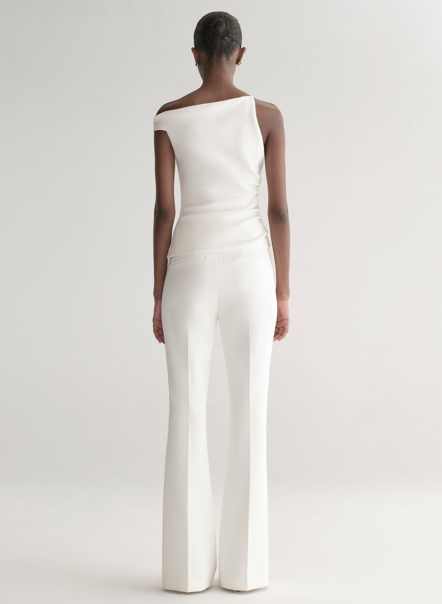 Woman wearing a white one-shoulder top and white pants on a plain background