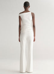 Woman wearing a white one-shoulder top and white pants on a plain background