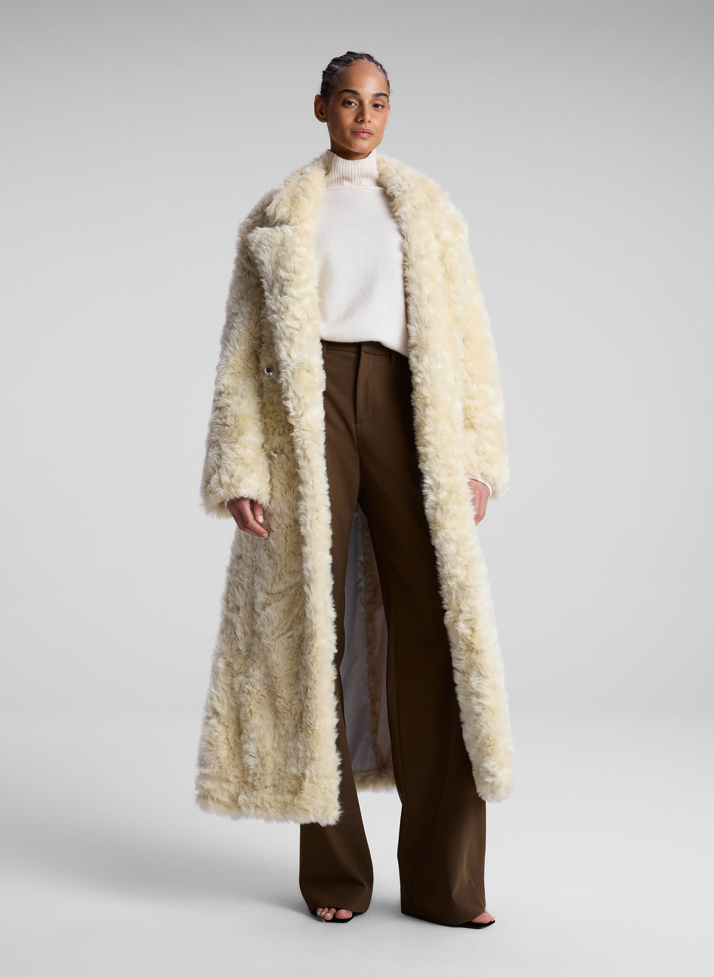 woman wearing cream faux fur coat, white turtleneck sweater and brown pants