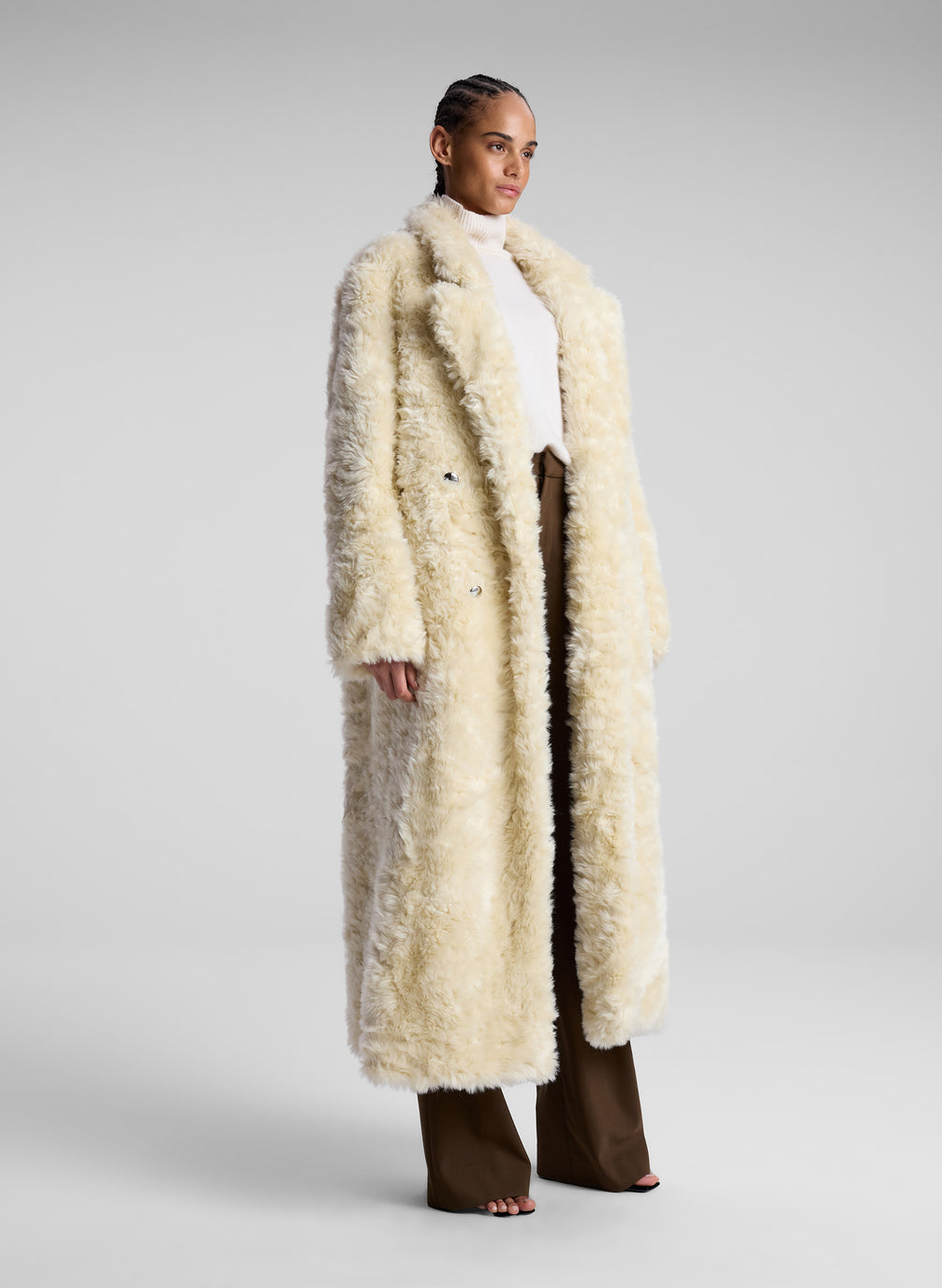 woman wearing cream faux fur coat, white turtleneck sweater and brown pants