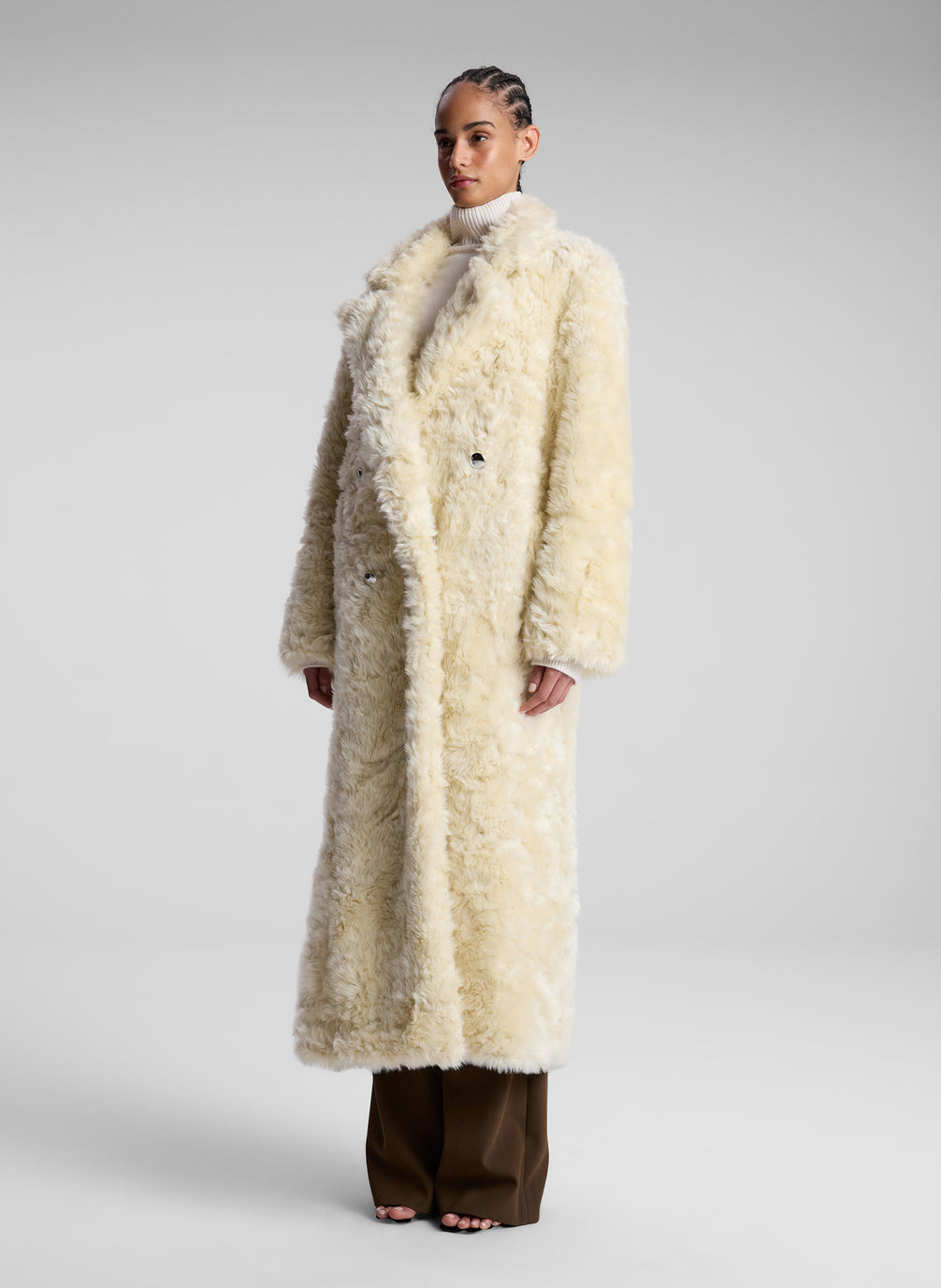 woman wearing cream faux fur coat, white turtleneck sweater and brown pants