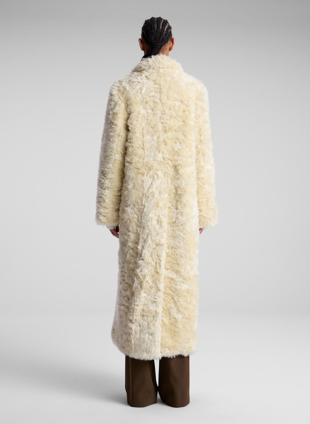 woman wearing cream faux fur coat, white turtleneck sweater and brown pants