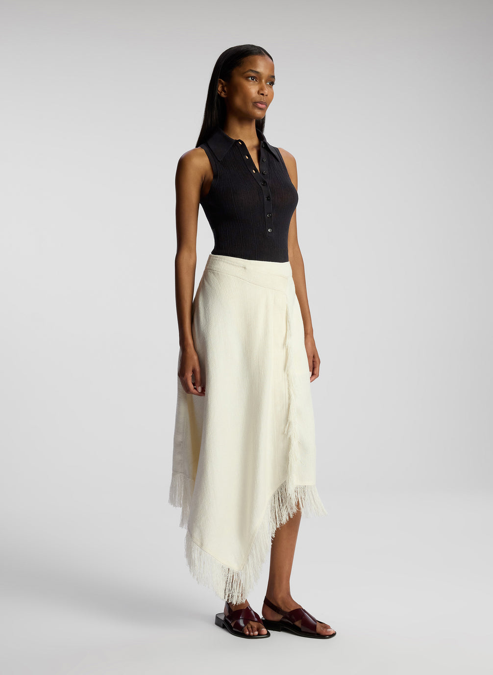 side view of woman wearing black collared sleeveless shirt and white skirt