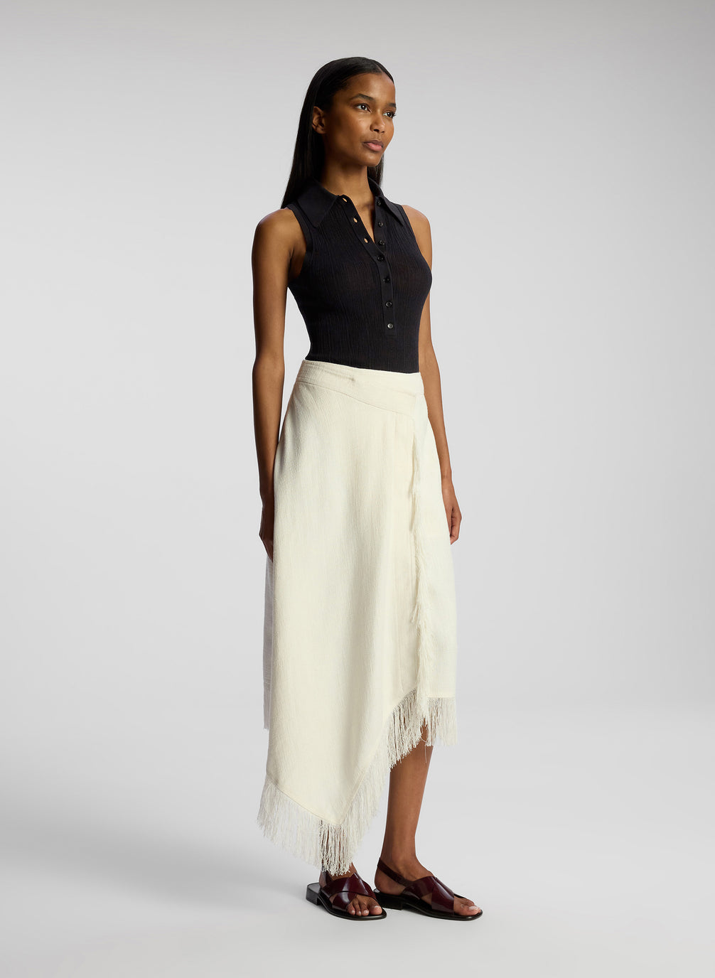 side view of woman wearing black collared sleeveless shirt and white skirt