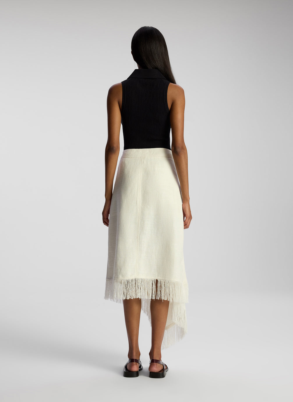 back view of woman wearing black collared sleeveless shirt and white skirt