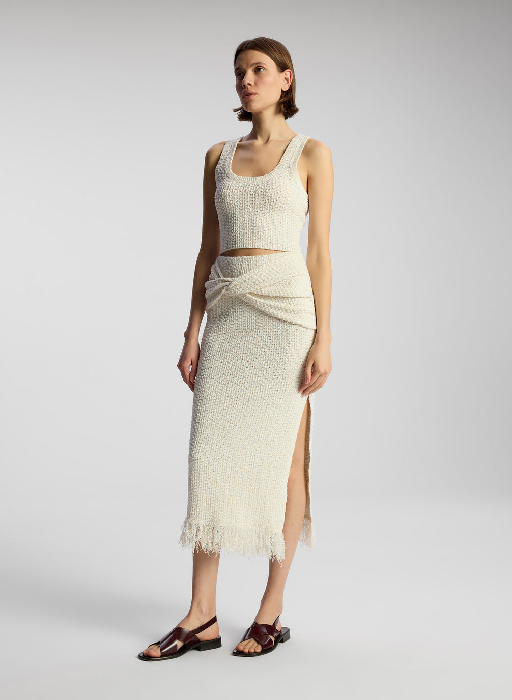 side view of woman wearing white knit sleeveless top and matching skirt