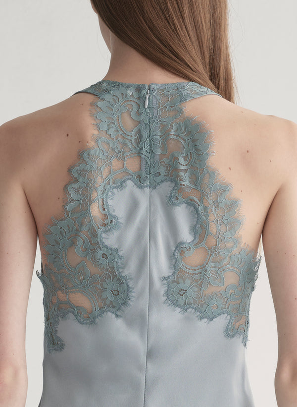 Woman wearing a light blue sleeveless top with lace details  and light blue pants on a plain background