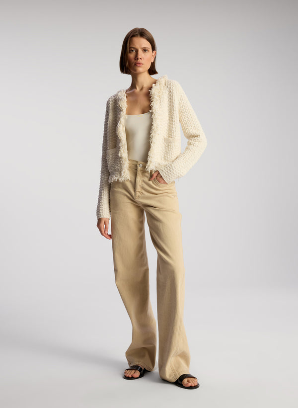 front view of woman wearing cream fringed cardigan and tan pants