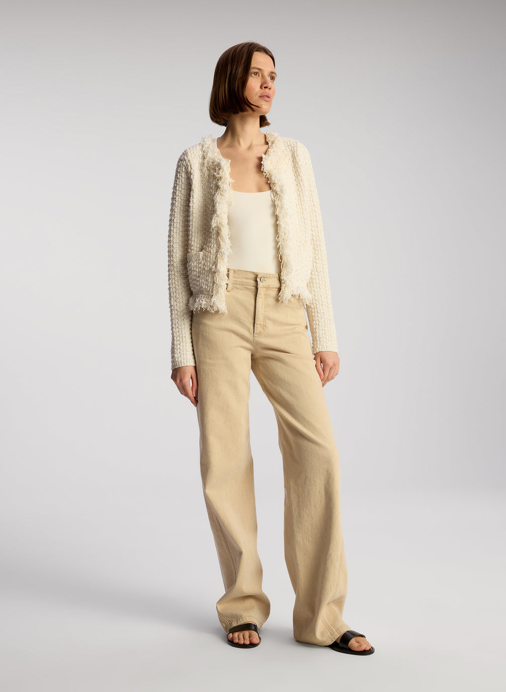 side view of woman wearing cream fringed cardigan and tan pants