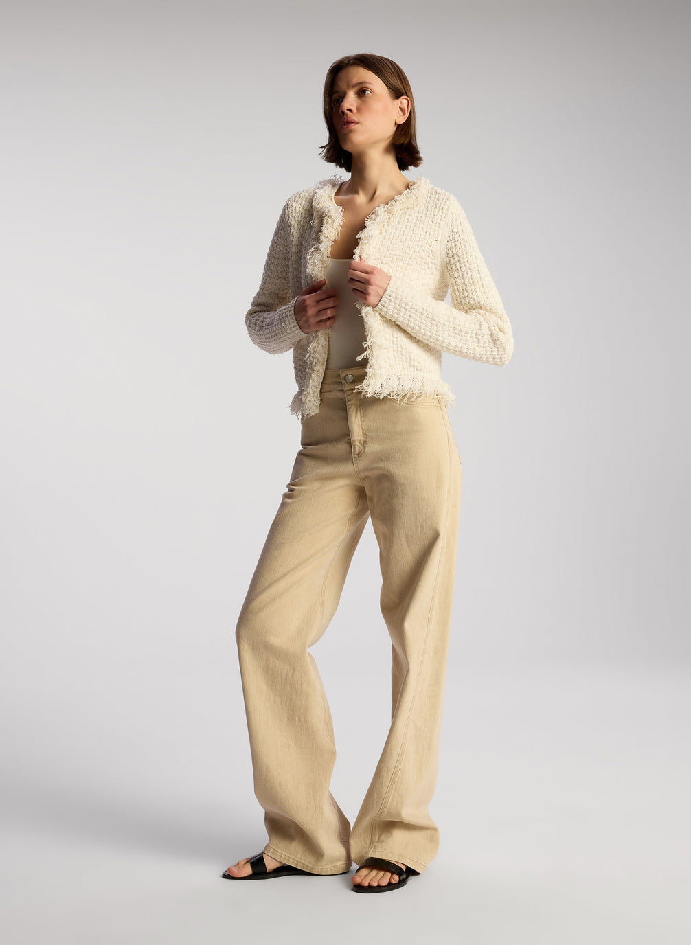 side view of woman wearing cream fringed cardigan and tan pants