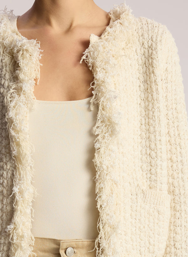 detail view of woman wearing cream fringed cardigan and tan pants