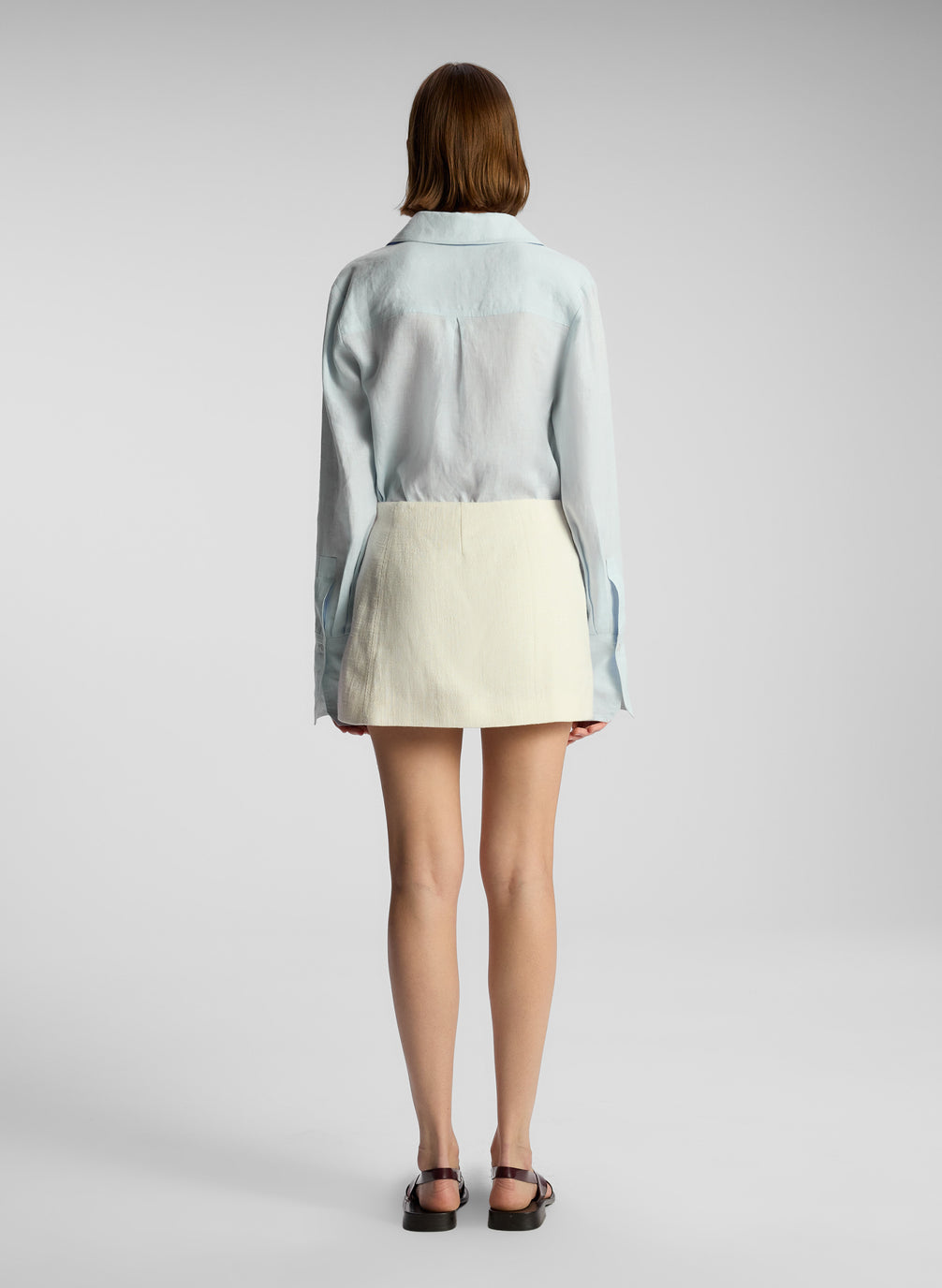 back view of woman wearing light blue button down and cream fringed mini skirt