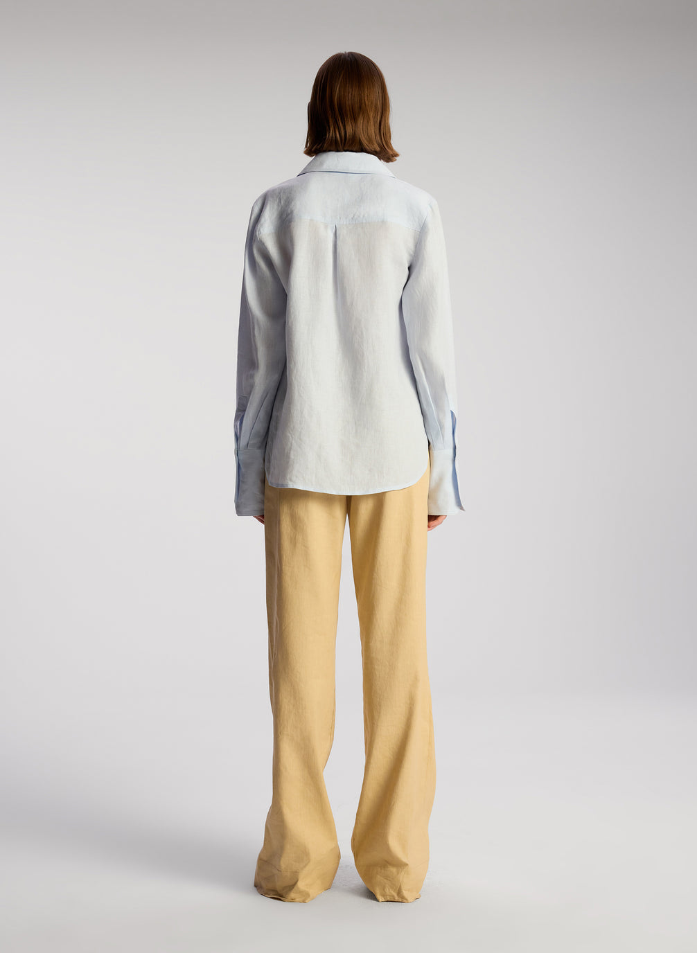 back view of woman wearing light blue linen button down shirt and tan pants