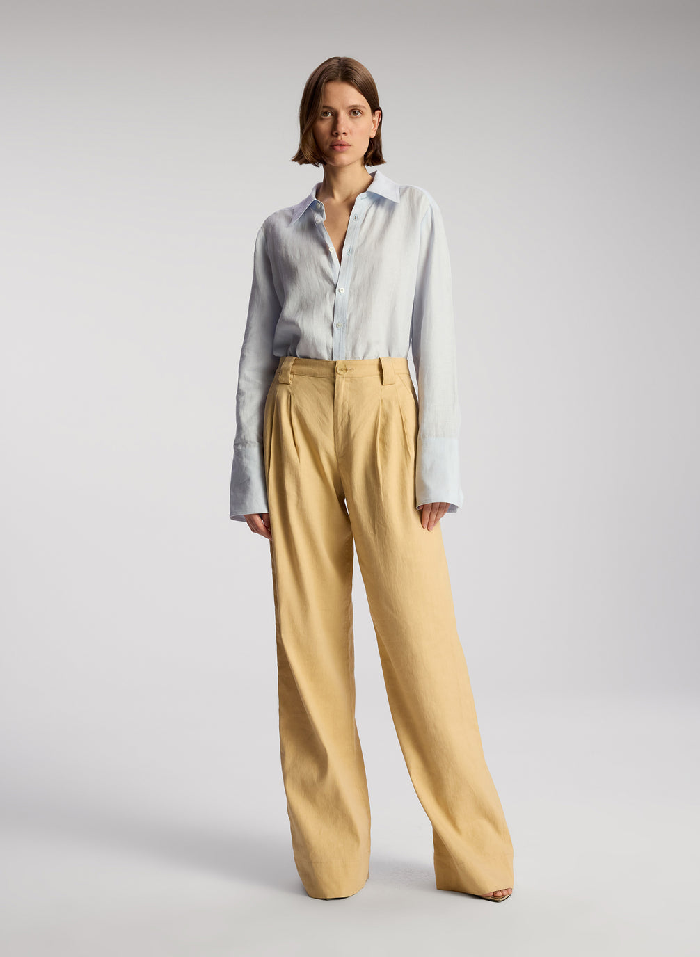 front view of woman wearing light blue linen button down shirt and tan pants