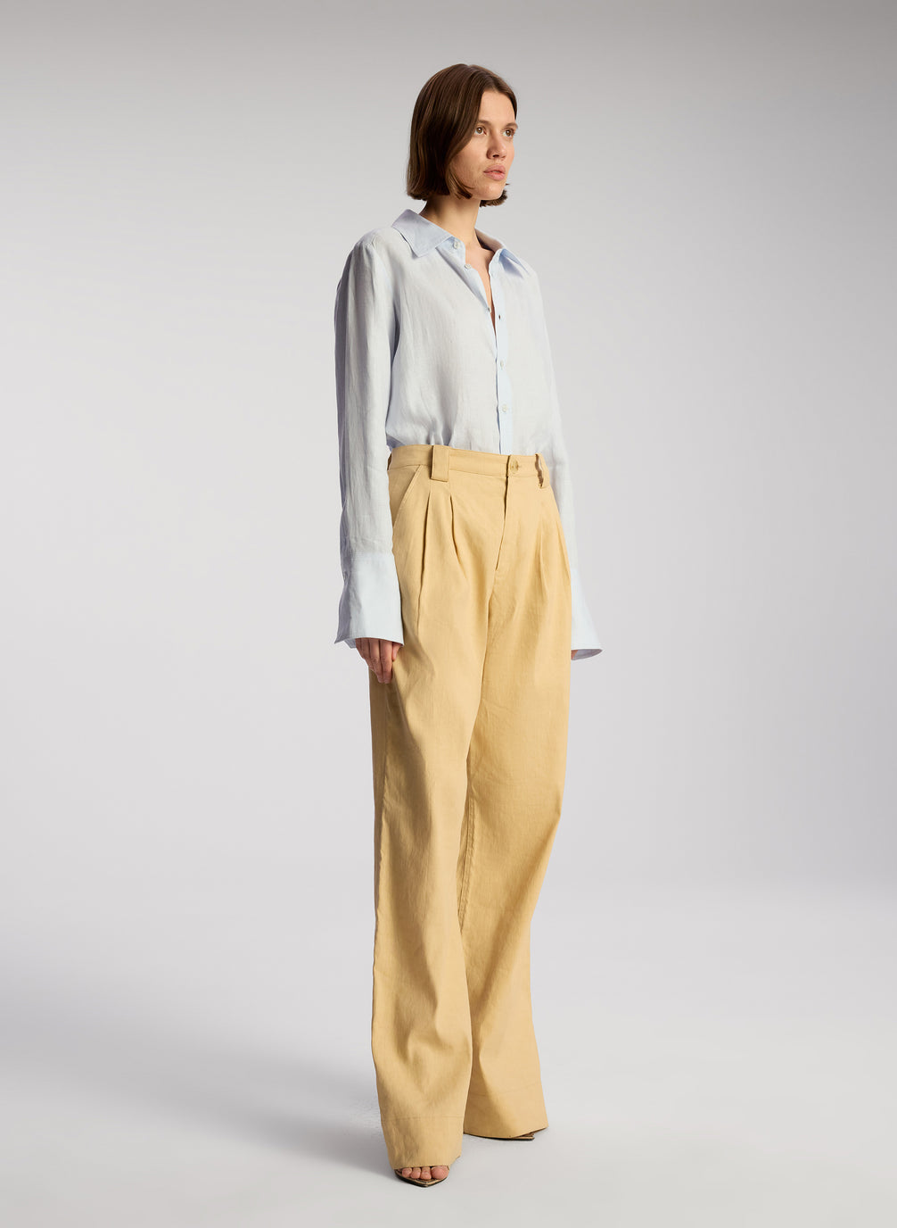 side view of woman wearing light blue linen button down shirt and tan pants