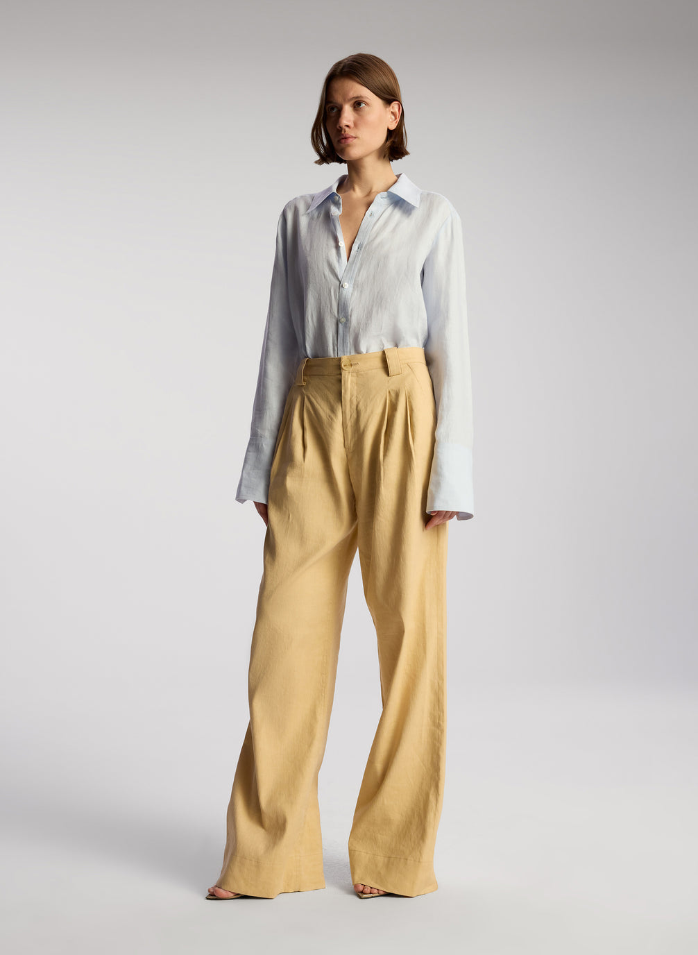 side view of woman wearing light blue linen button down shirt and tan pants