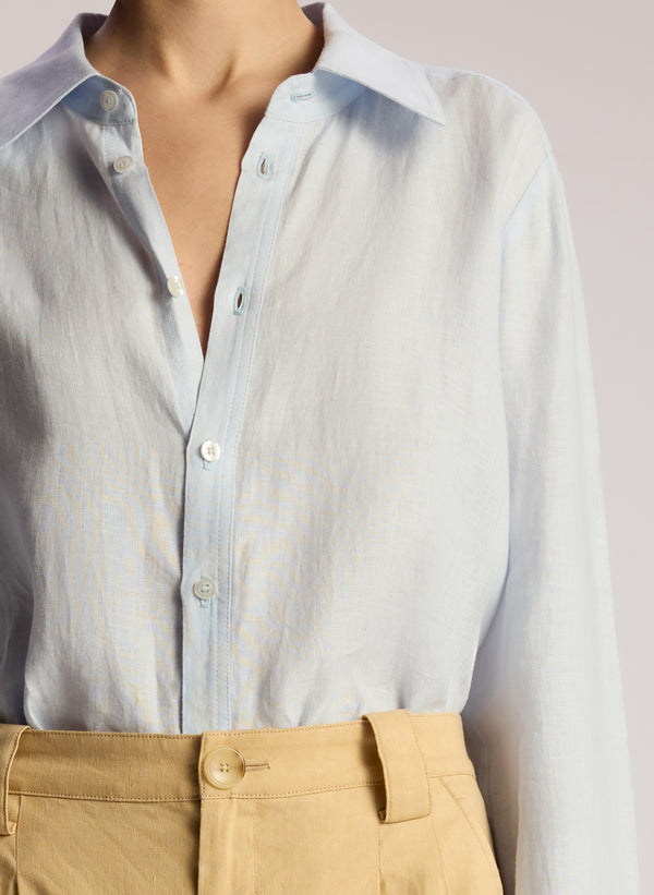 detail view of woman wearing  light blue linen button down shirt and tan pants