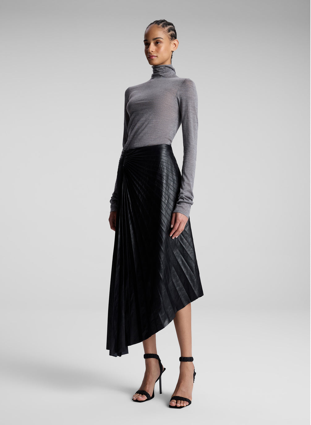 woman wearing grey turtleneck and black vegan leather pleated skirt