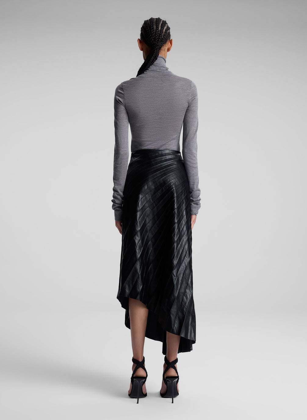 woman wearing grey turtleneck and black vegan leather pleated skirt