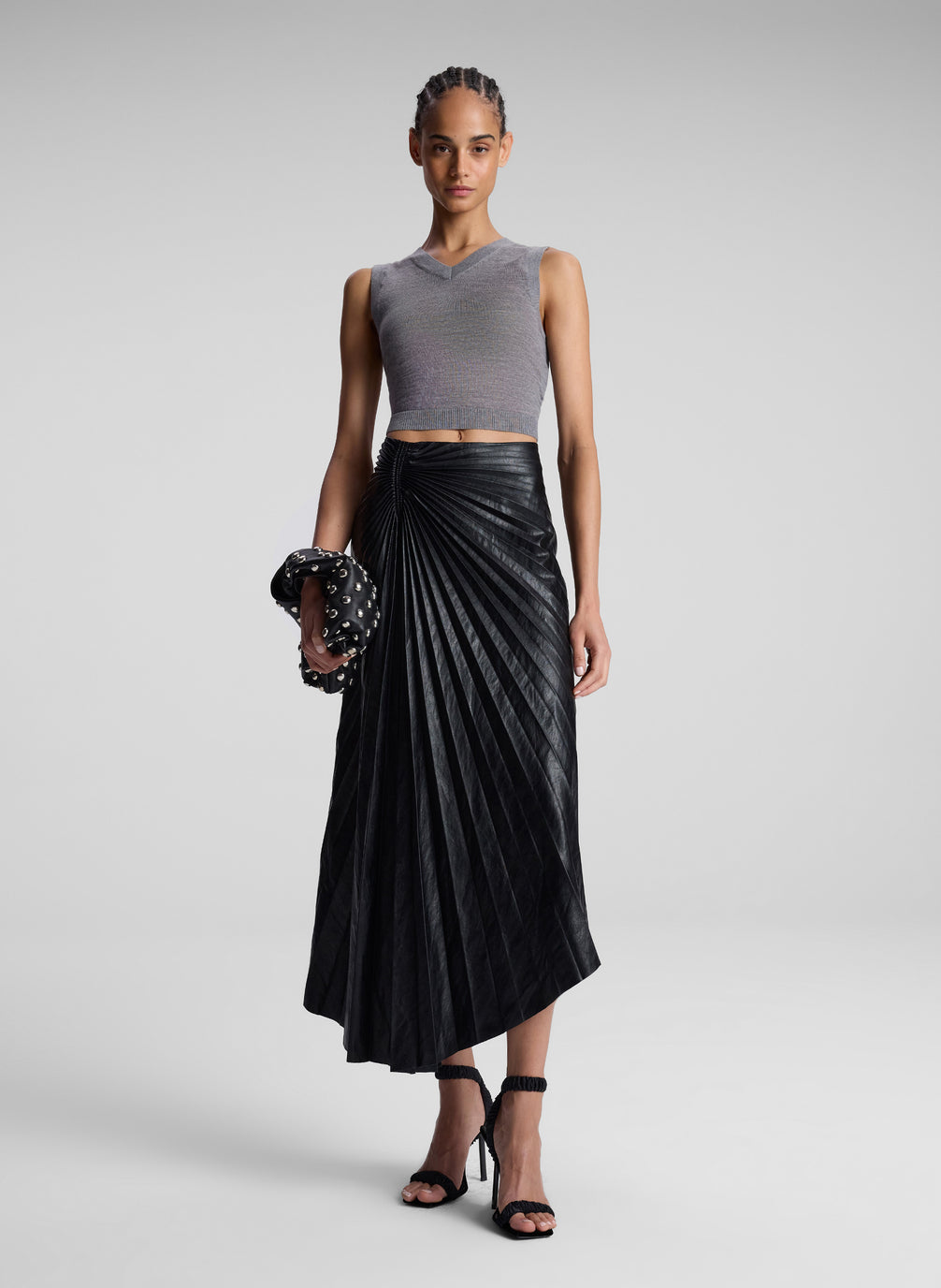 woman wearing grey knit vest and black pleated vegan leather skirt