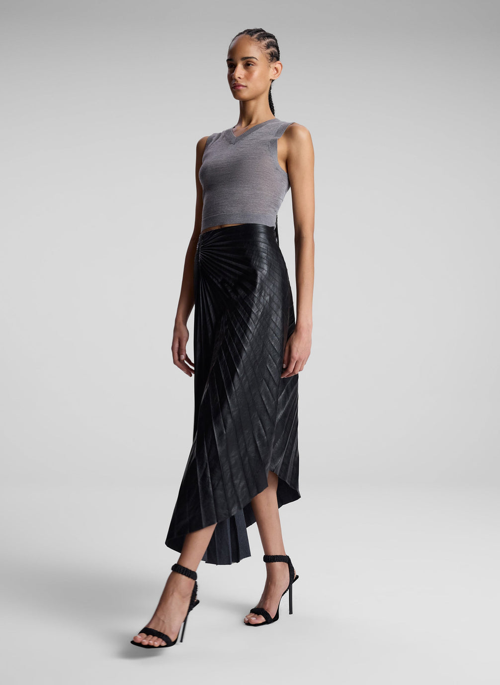 woman wearing grey knit vest and black pleated vegan leather skirt