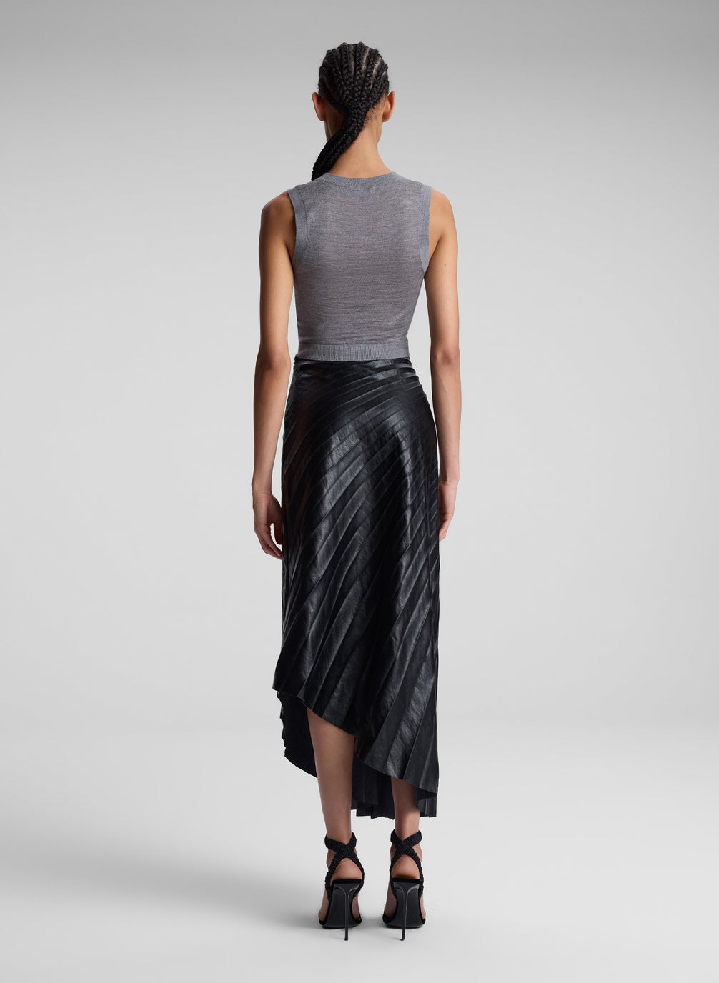 woman wearing grey knit vest and black pleated vegan leather skirt