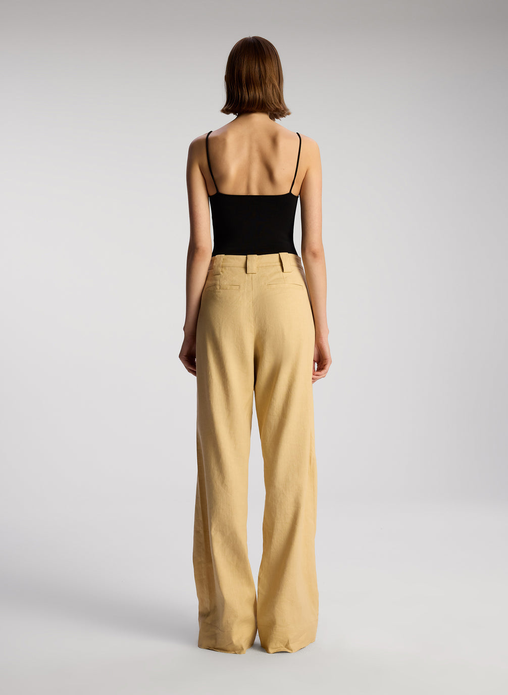 back view of woman wearing black sleeveless bodysuit and tan pants