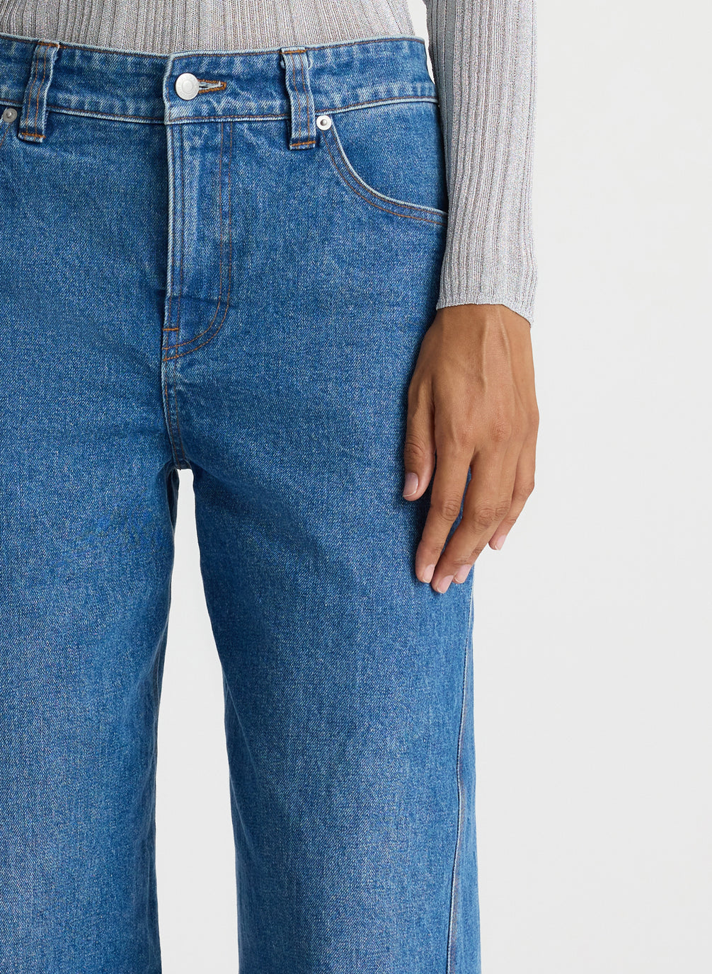 detail of front view of woman in silver long sleeve top and medium blue wash jeans