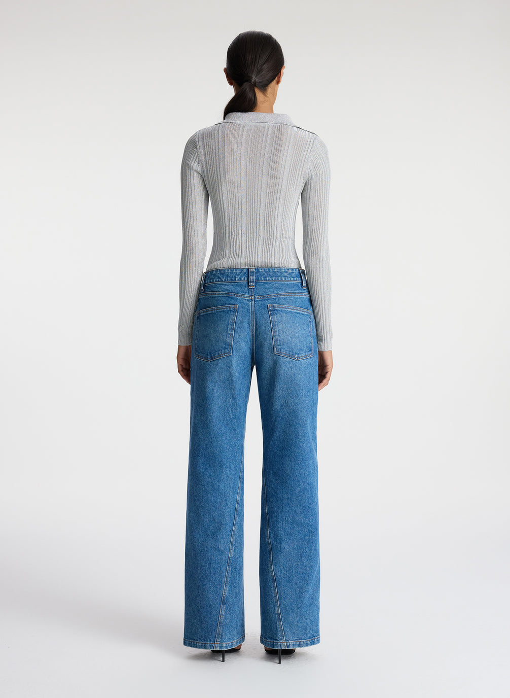 back view of woman in silver long sleeve top and medium blue wash jeans