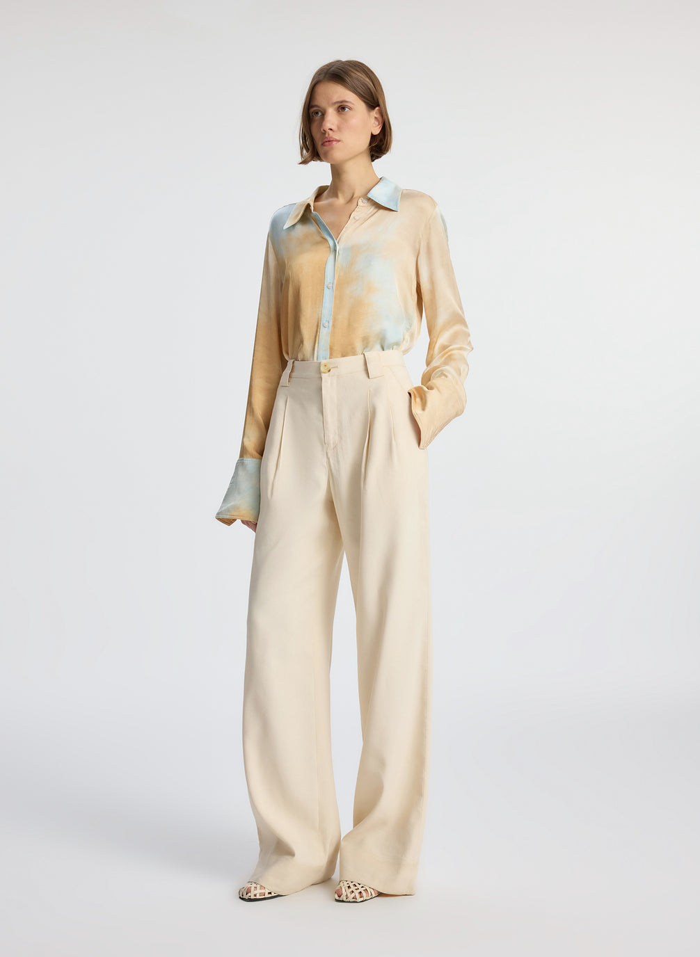 side view of woman wearing long sleeve collared multicolored shirt and beige pants