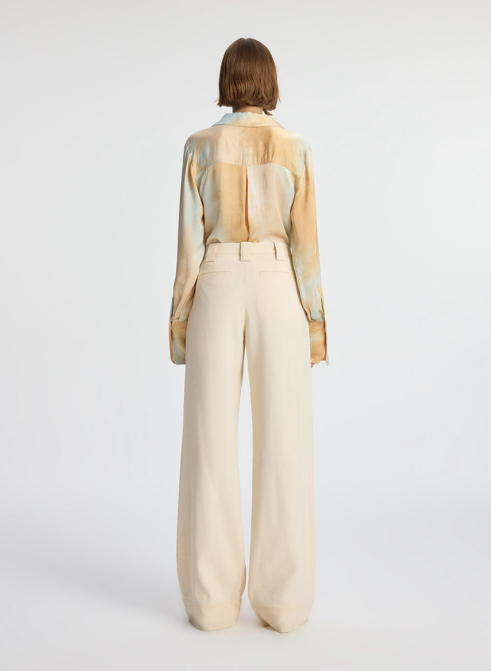back view of woman wearing long sleeve collared multicolored shirt and beige pants