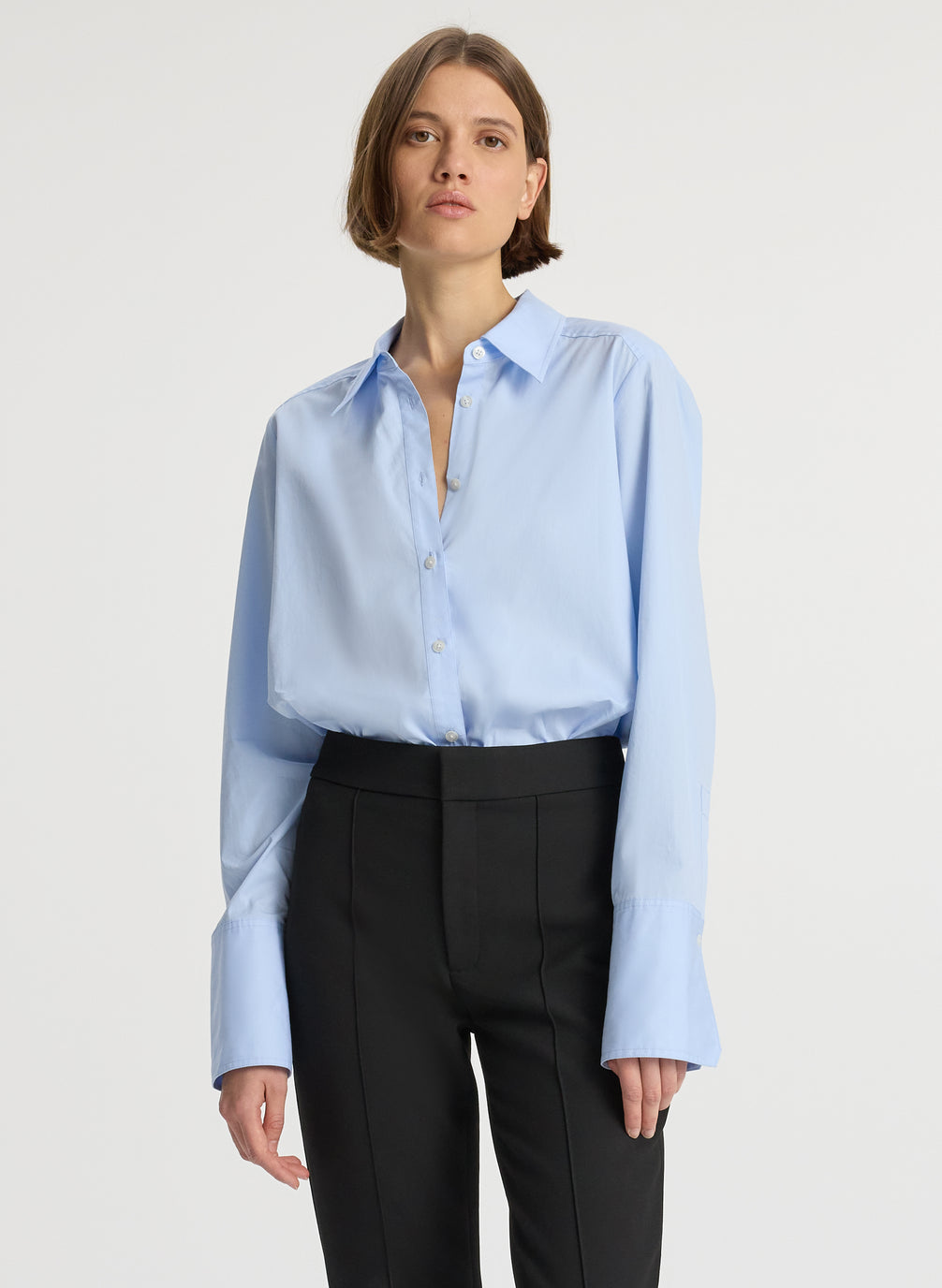 detail view of woman wearing light blue button down collared shirt and black ankle length pants