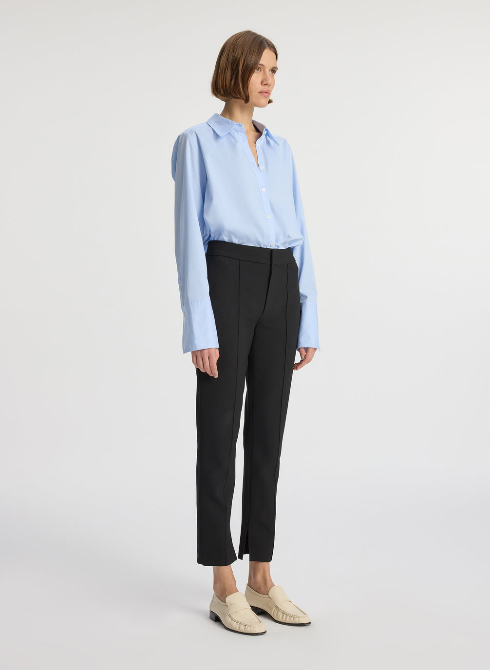 side view of woman wearing light blue button down collared shirt and black ankle length pants