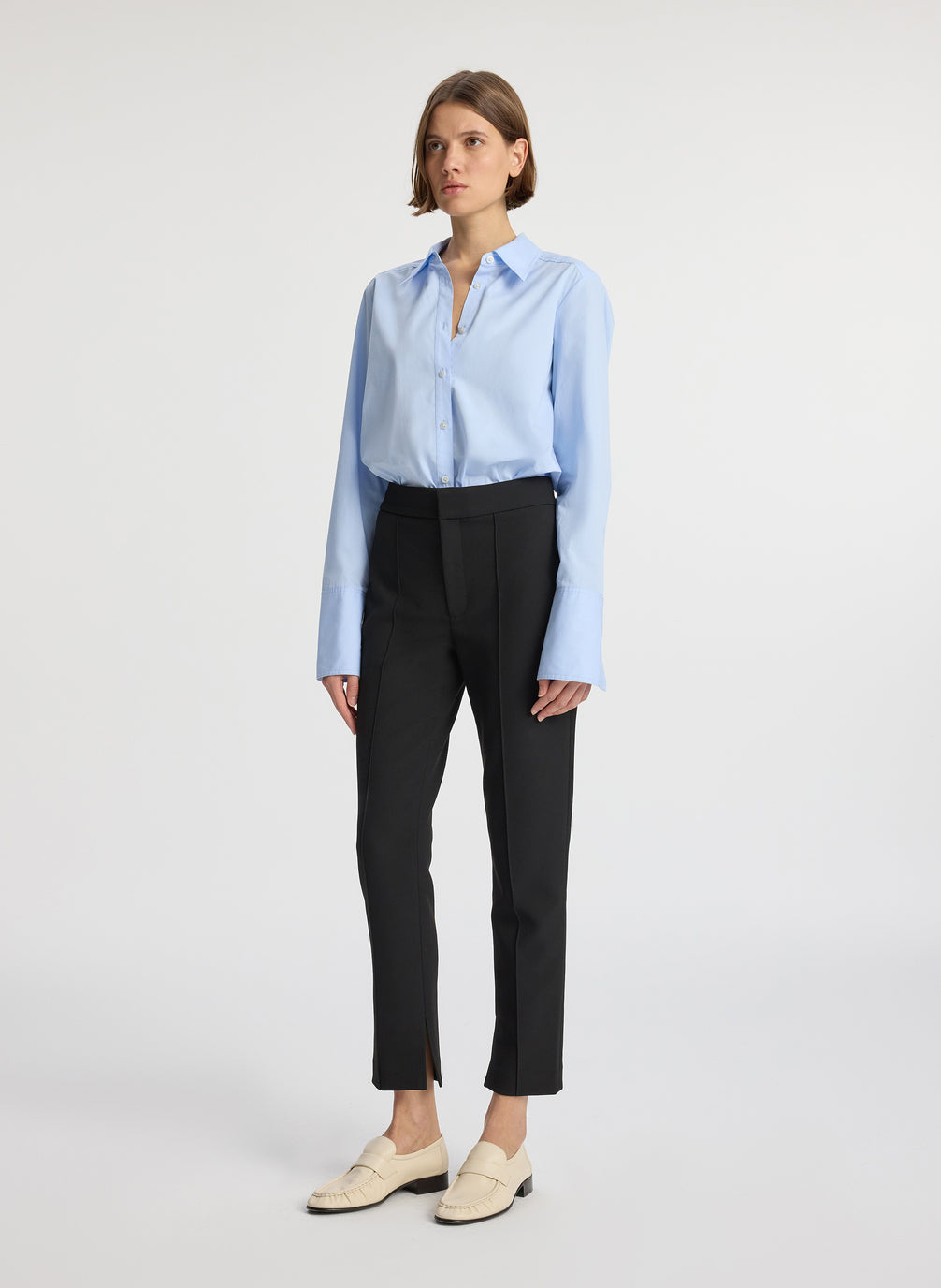 side view of woman wearing light blue button down collared shirt and black ankle length pants