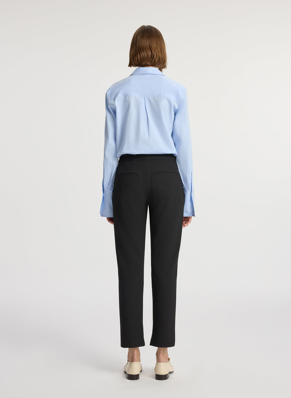 back view of woman wearing light blue button down collared shirt and black ankle length pants