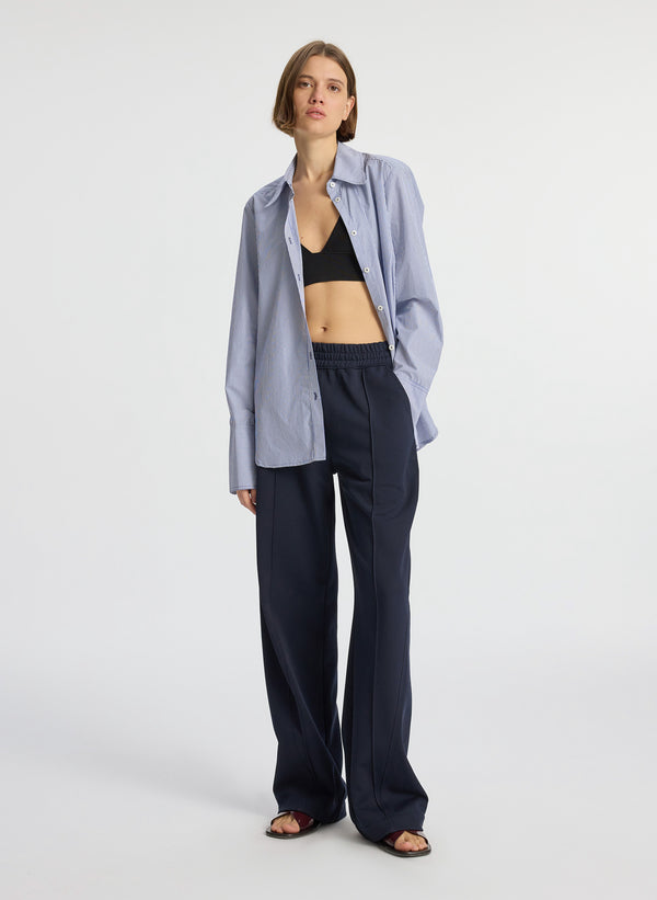 front view of woman wearing blue striped unbuttoned shirt black knit bra and navy blue pants