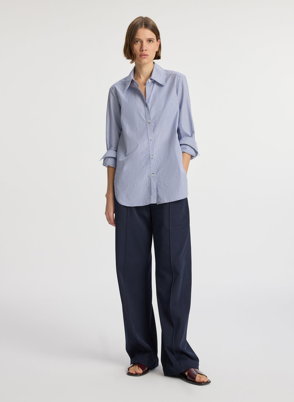 front view of woman wearing blue striped button down collared shirt and navy blue pants