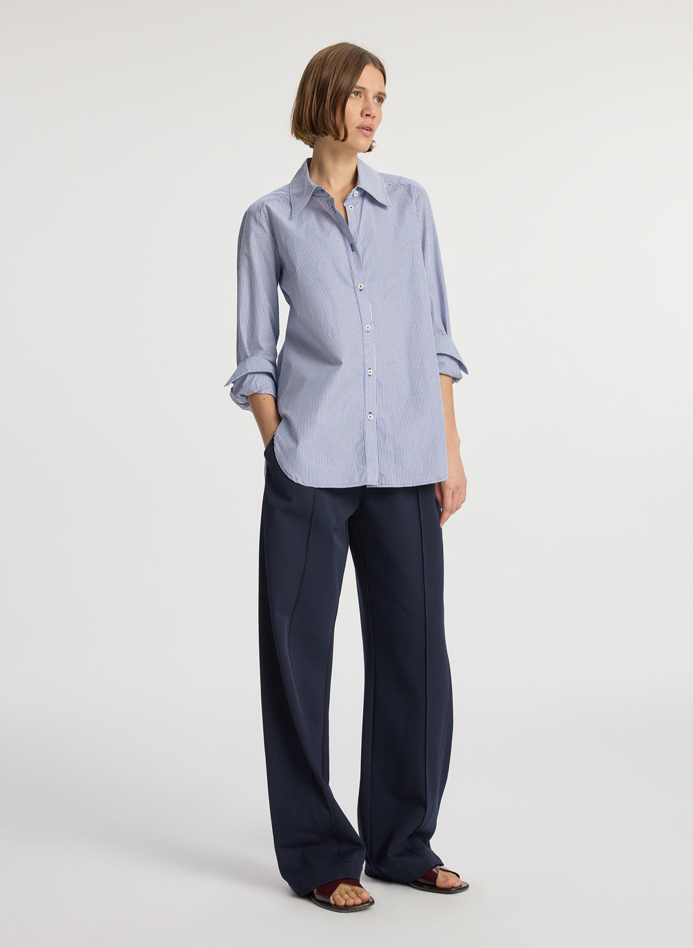 side view of woman wearing blue striped button down collared shirt and navy blue pants