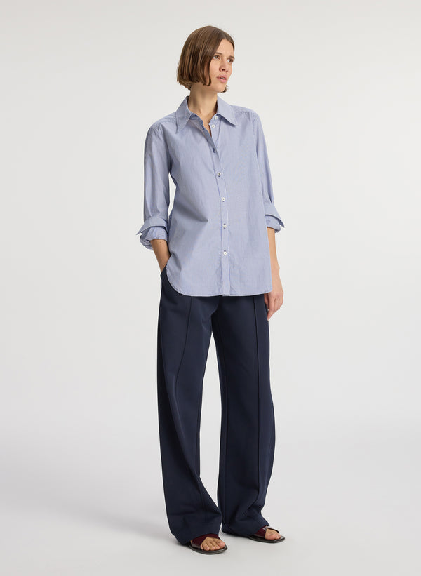 side view of woman wearing blue striped button down collared shirt and navy blue pants