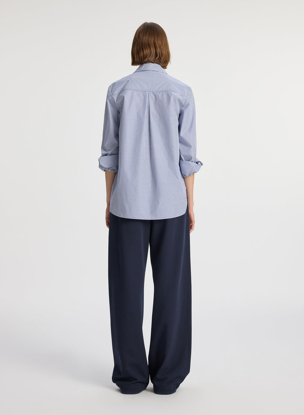 back view of woman wearing blue striped button down collared shirt and navy blue pants