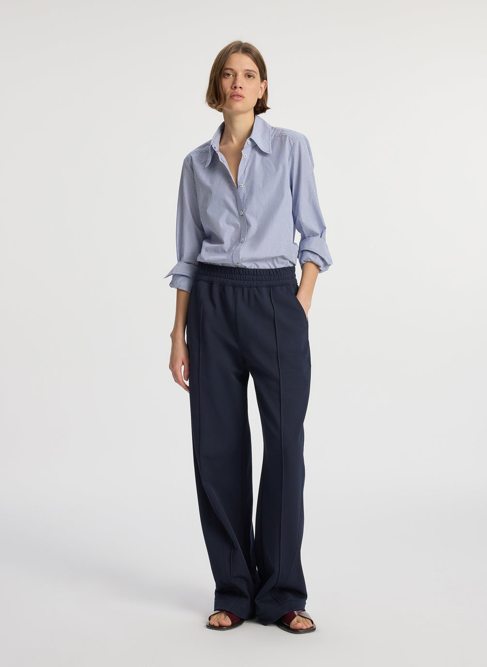 front view of woman wearing blue striped button down collared shirt and navy blue pants